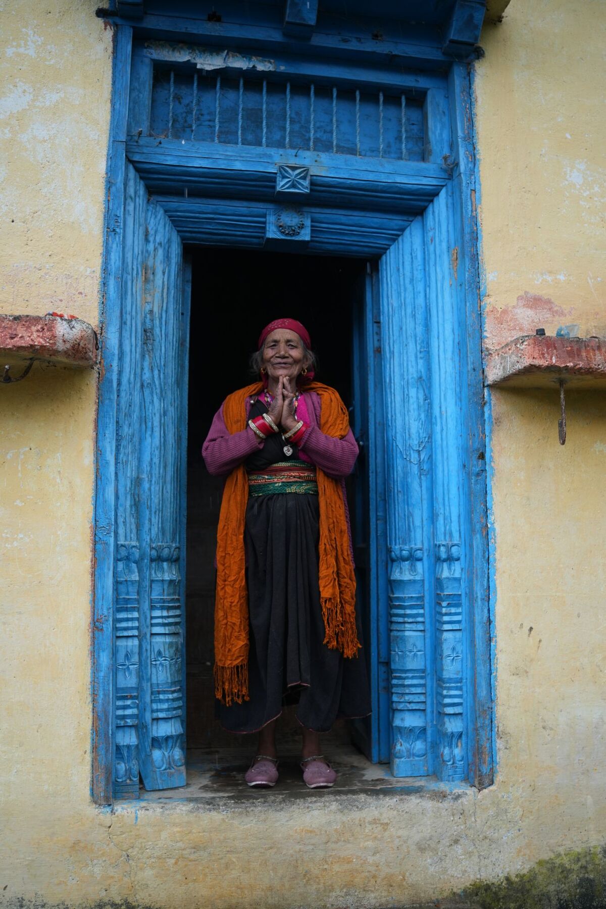 Smiling woman in traditional dress greeting with folded hands in a blue carved wooden doorway
