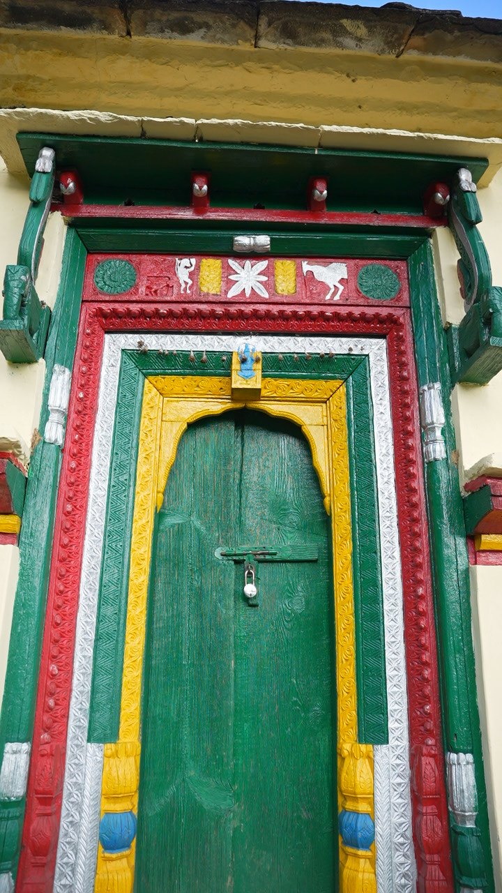 A carved wooden door frame painted in green, red, yellow and silver around a padlocked green door