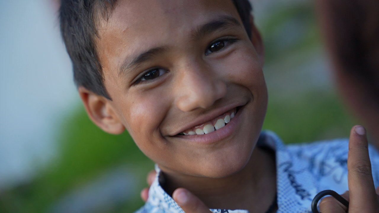 A smiling boy in a patterned blue and white shirt, looking at the camera
